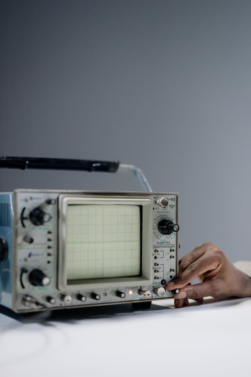 Hand adjusting a control on a real analog oscilloscope with a blank screen.