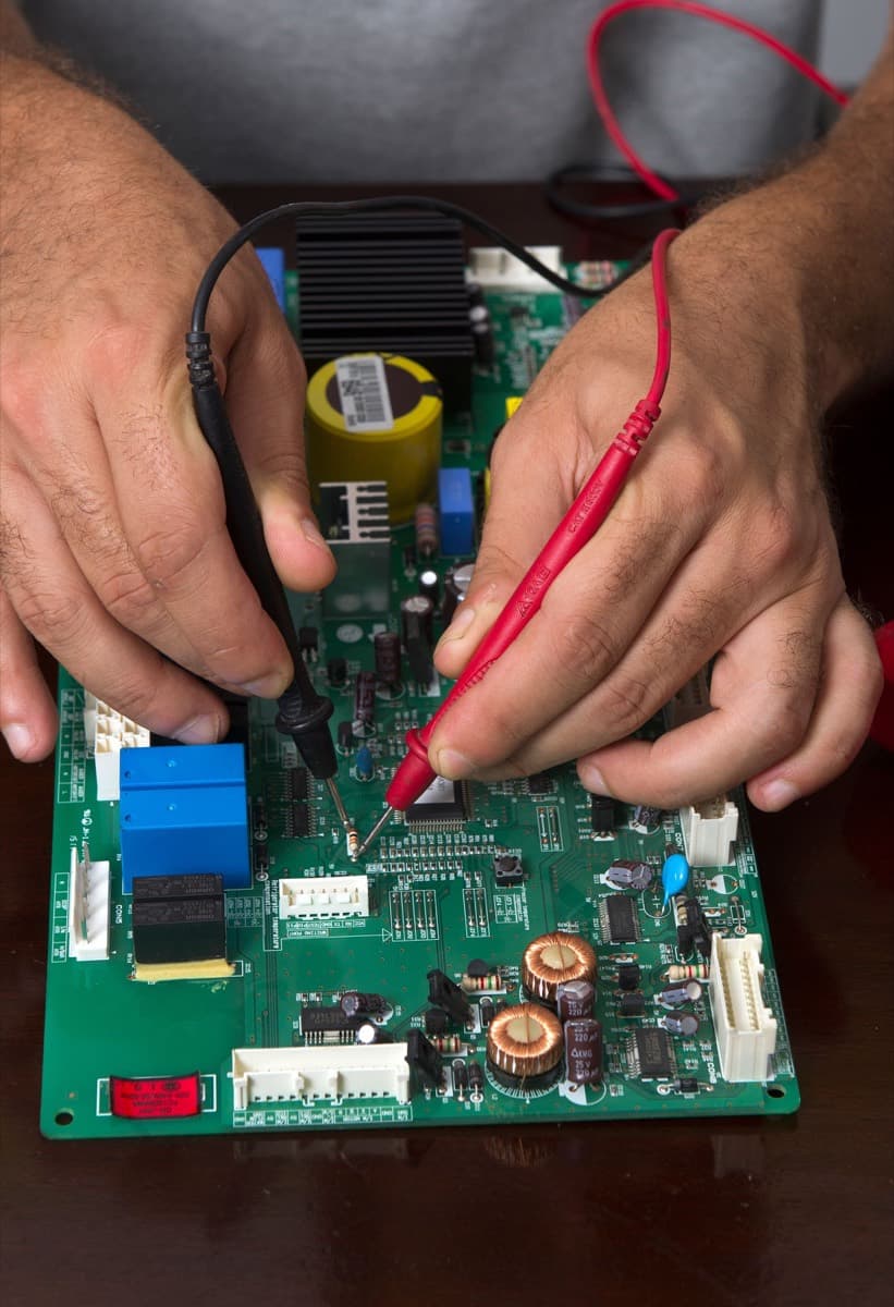 Hands making generic meter-probe contact on a real circuit board.