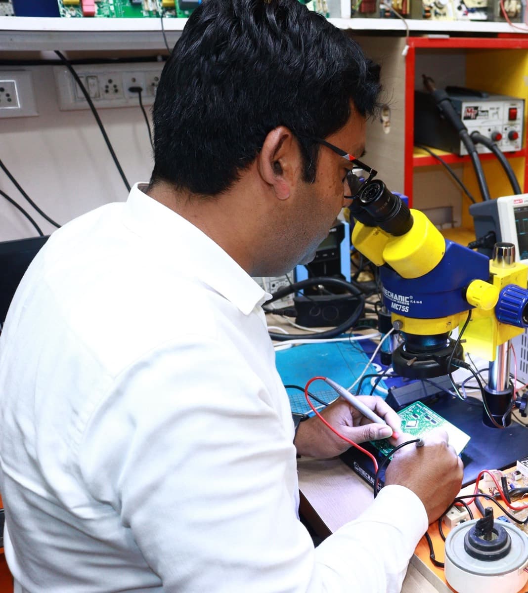 Technician inspecting a circuit board through a microscope in a real electronics workshop.